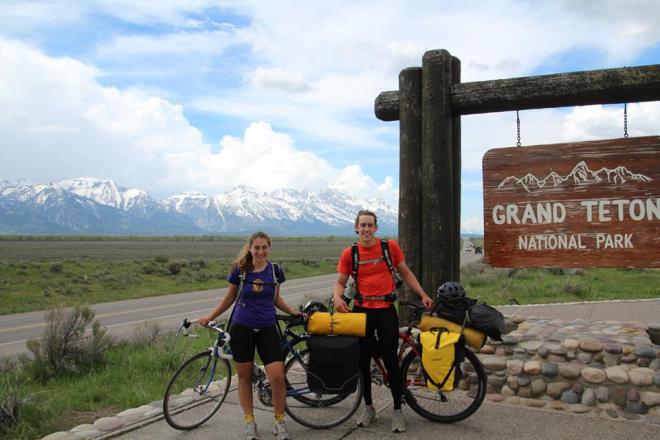 Maia Wellborn (left) and Alex Aboutanos (right) stand at the Grand Teton National Park entrance sign during their May 2014 3-week, 600-mile bike tour in the west.